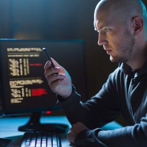IT-tekniker med mobil i handen framför datorskärmar.