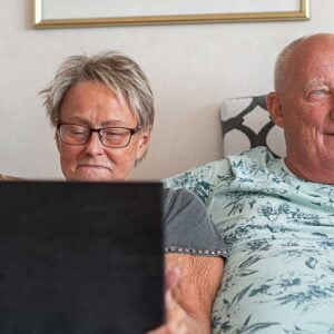 Två seniorer sitter i soffa med en bärbar dator framför sig.