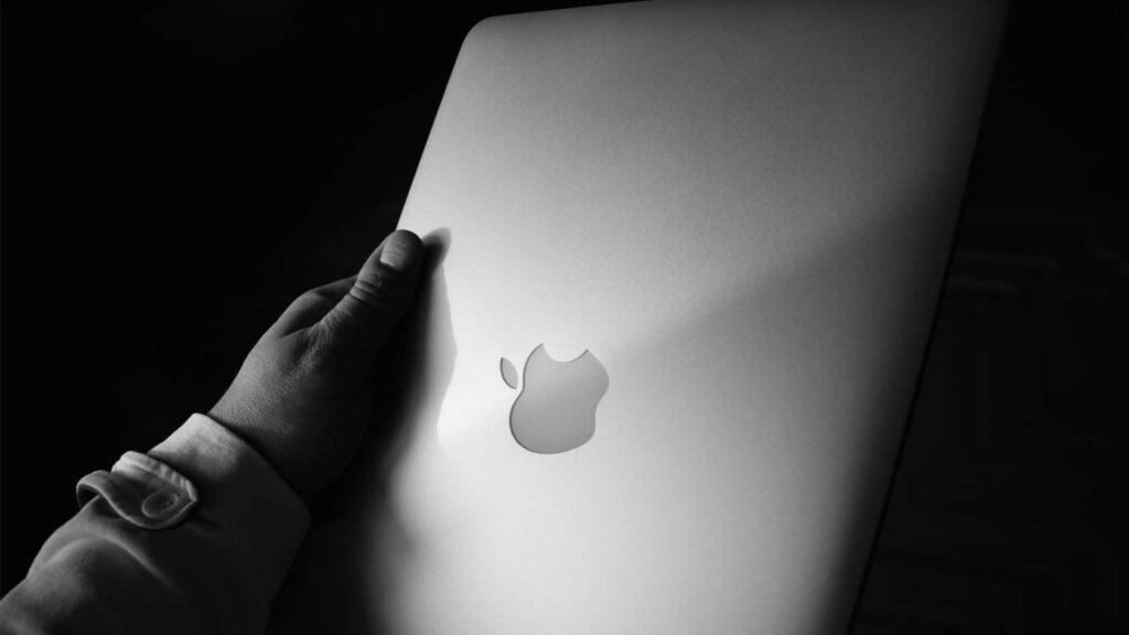 Svartvitt fotografi av en hand som håller en äldre Macbook.