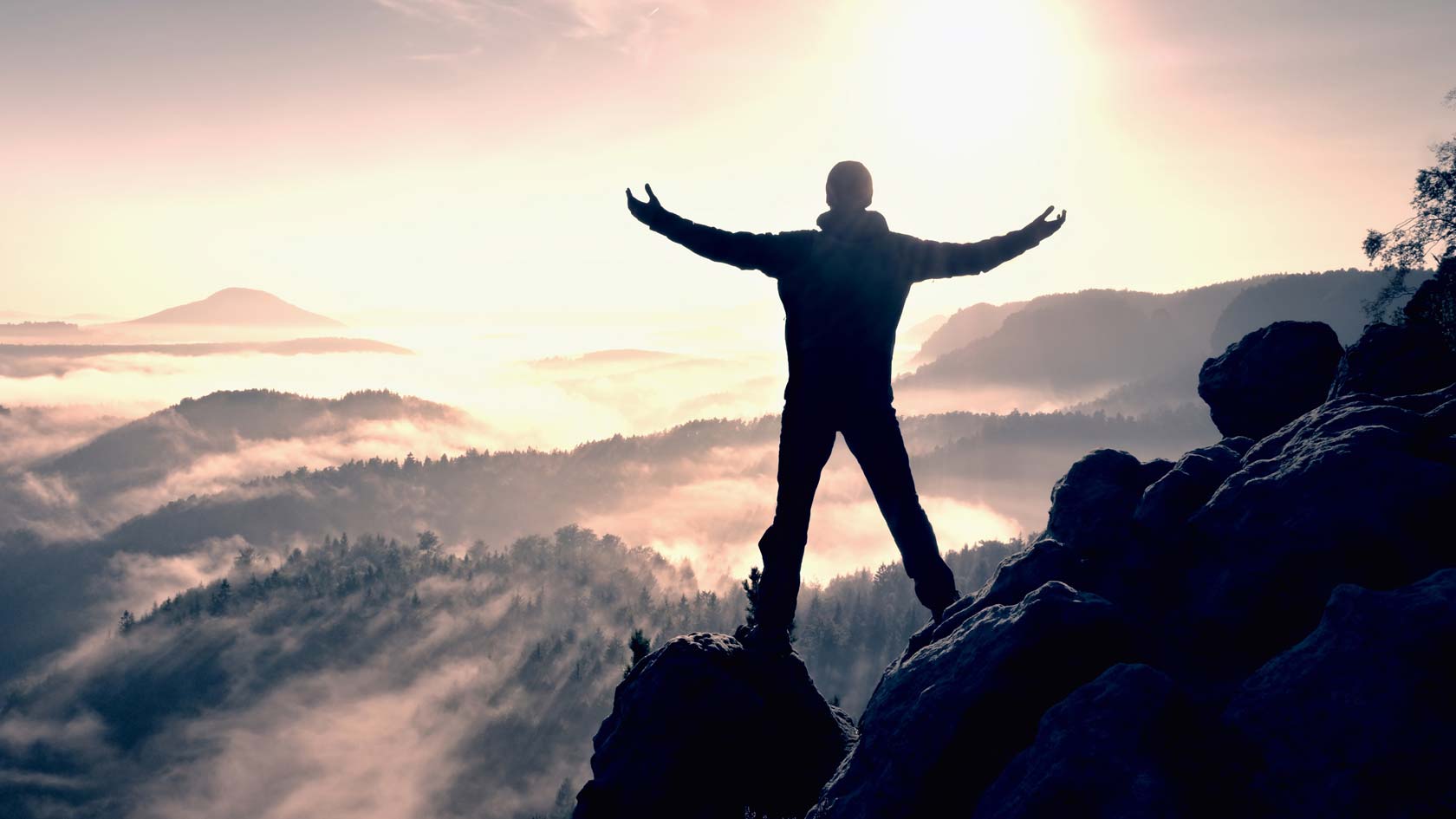 En ensam person står på toppen av ett berg. Personen har en segermässig hållning..