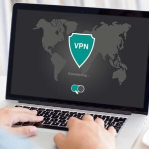 Person sitter vid sin dator med en kopp kaffe intill. På datorn visas en generisk logotyp där det står VPN.
