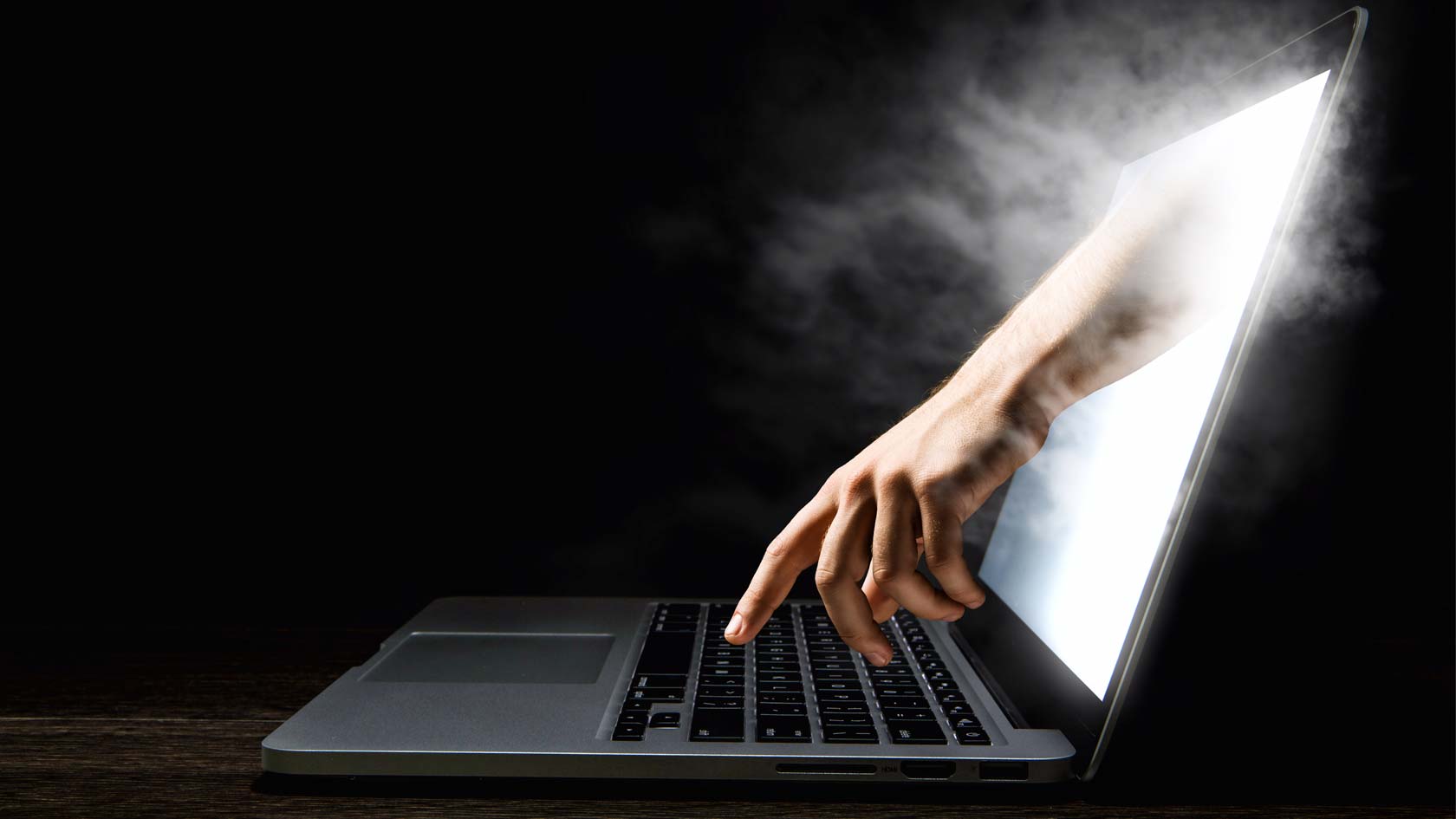 En hand sträcker sig genom skärmen på en bärbar dator och sträcker sig efter tangentbordet.