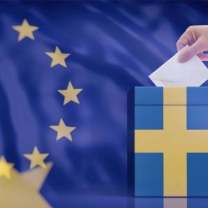 Person lägger röstsedel i en låda med Sveriges flagga. I bakgrunden syns EU-flaggan.