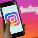 En person håller upp en mobil med Instagrams ikon. Texten ”Instagram” syns svagt i bakgrunden.