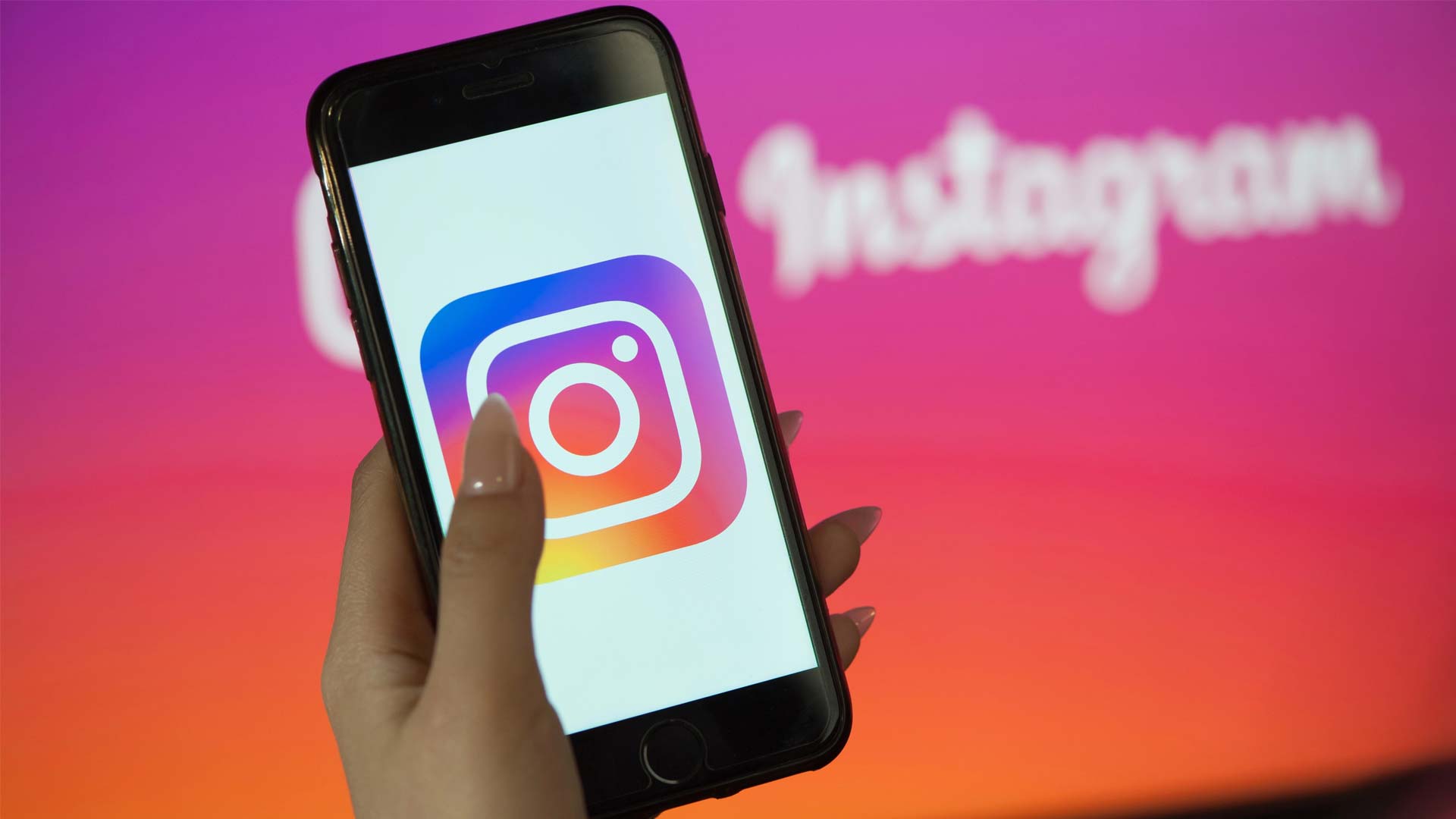 En person håller upp en mobil med Instagrams ikon. Texten ”Instagram” syns svagt i bakgrunden.