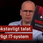 Karl Emil Nikka håller upp boken Millenniumskandalen. Texten ”ett bokstavligt talat livsfarligt IT-system” är stämplad ovanpå.