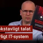 Karl Emil Nikka håller upp boken Millenniumskandalen. Texten ”ett bokstavligt talat livsfarligt IT-system” är stämplad ovanpå.