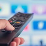 En person håller en tv-fjärrkontroll riktad mot en smart-tv.