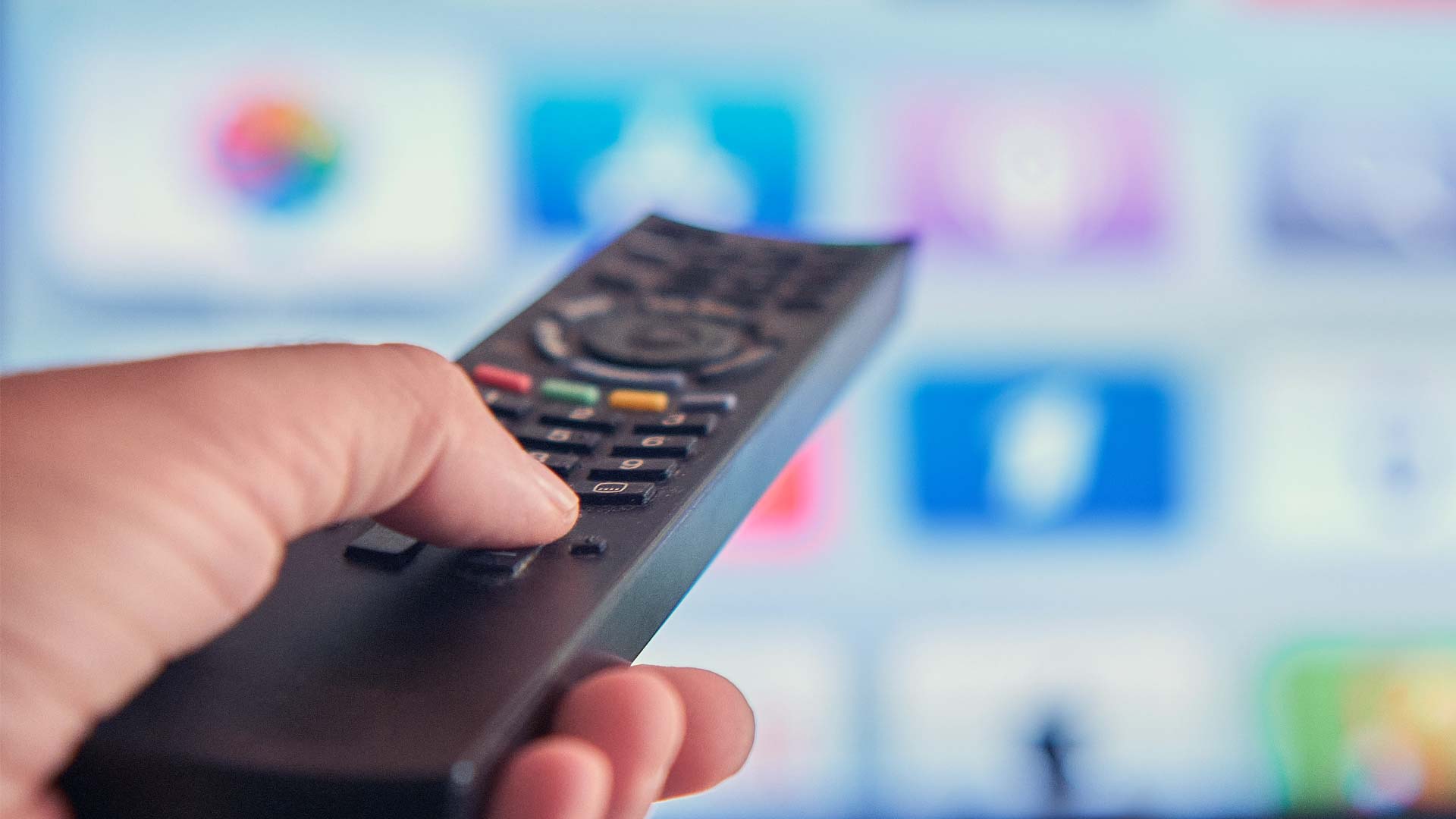 En person håller en tv-fjärrkontroll riktad mot en smart-tv.